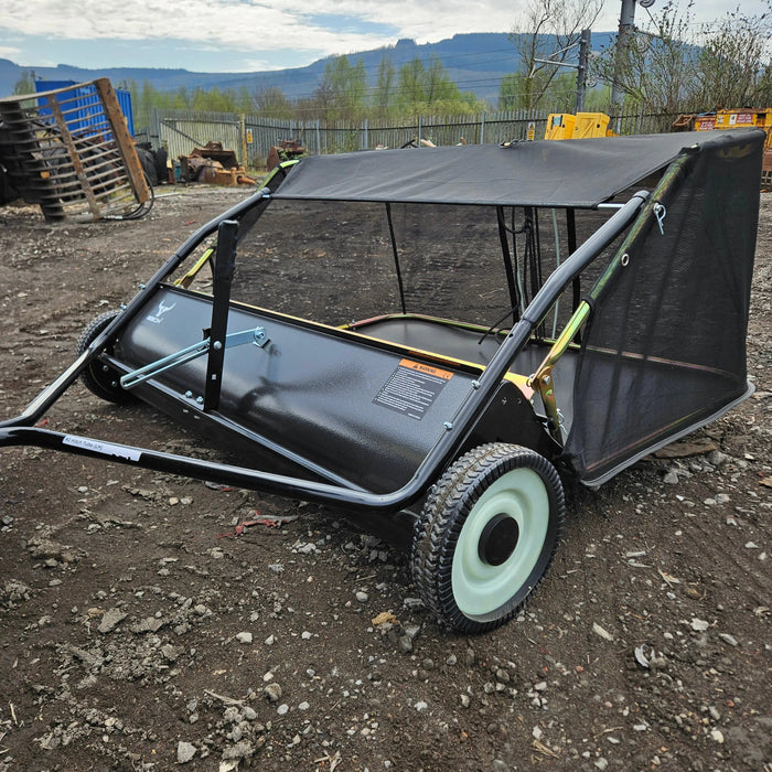 A Tow-Behind Lawn Sweeper 48" – Heavy-Duty Leaf, Grass & Debris Collector for Riding Mowers, Tractors & ATVs stands on a gravel surface outdoors.