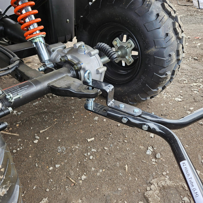 Close-up of an off-road vehicle's rear suspension, wheel, and hitch assembly on gravel—perfect for attaching the Tow-Behind Lawn Sweeper 48", a heavy-duty leaf, grass & debris collector for riding mowers, tractors & ATVs.