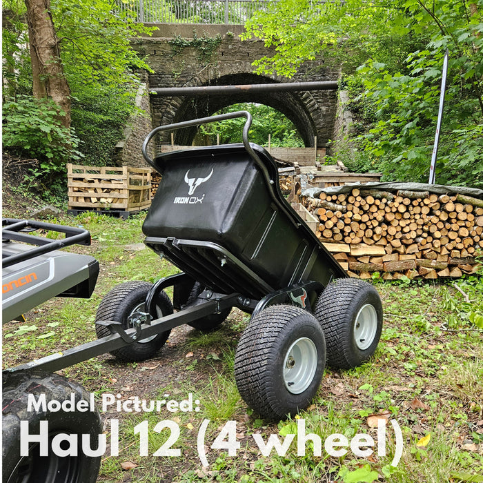 The Iron Ox® Haul 12 - Tipping Trailer 1200lb 4-Wheel is shown on a forested path near stacked firewood, featuring a corrosion-resistant bed with a stone bridge in the background.