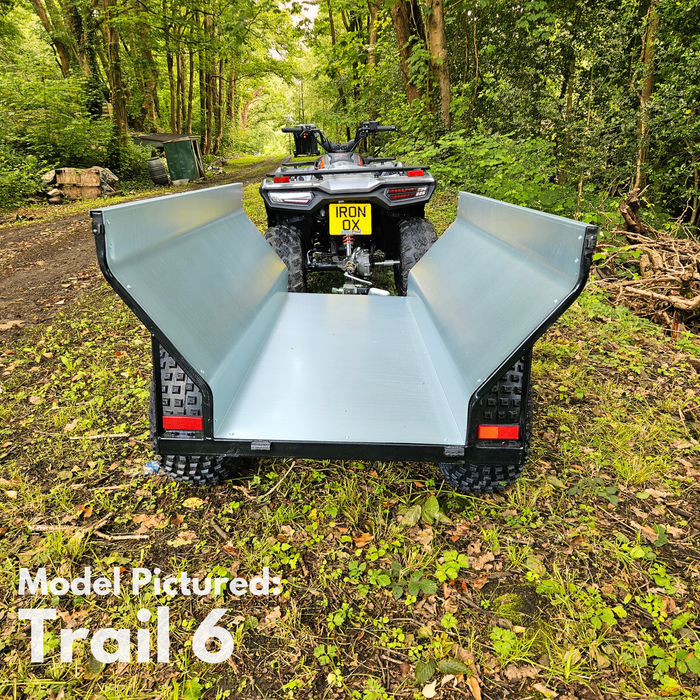 An all-terrain vehicle is parked on a forest path, towing the All-Terrain ATV & Farm Tipping Trailer | Heavy-Duty Utility Trailer - Trail 6 with raised side panels. Text reads: "Model Pictured: Trail 6.