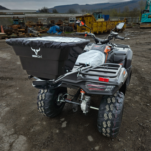 ATV Quad bike with a black seed feed fertiliser spreader attached to the back, set in an outdoor environment with industrial background.