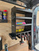 The Van Racking Drill & Accessory Shelf for Garages, Workshop is a wall-mounted solution that optimizes van storage with a drill holder rack and shelves designed for spray cans, a spirit level, and pink cloths. Cordless drills are neatly arranged below, providing superior power tool storage that surpasses typical garage organization standards.