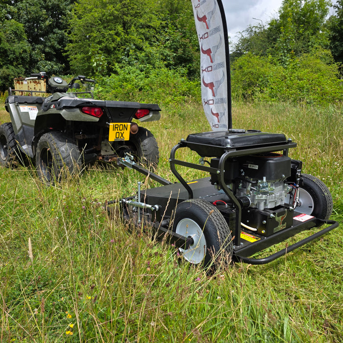 Quad bike towing a topper mower across a field during pasture maintenance.