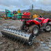 A red Towable Spiked Roller Aerator 60" Wide parked in a muddy area.